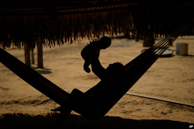 An Indigenous Juma youth holds a baby in a hammock in her community, near Canutama, Amazonas state, Brazil, Sunday, July 9, 2023. (AP Photo/Andre Penner)