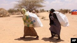 FILE - Southern Somali women carry food aid donations from the UNHCR as they make their way to their refugee camp in Dollow, Somalia, Aug. 30, 2011. Hunger is again stalking the country, and the U.N. is appealing for aid.