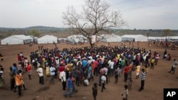 FILE - In this April 3, 2017, photo in the Imvepi camp, South Sudanese refugees gather under a tree from which names are announced for those allocated a land parcel from the Ugandan government. 