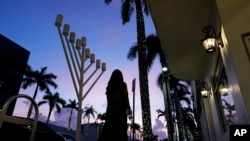 ARCHIVO - Una mujer vestida de forma conservadora pasa junto a una menorá frente a una sinagoga judía antes del inicio de Janucá, en Miami Beach, Florida, el viernes 1 de diciembre de 2023. 