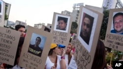 ARCHIVO - Manifestantes sostienen carteles de cartón que muestran imágenes de familiares y amigos asesinados durante protestas antigubernamentales, en Caracas, Venezuela, el 18 de marzo de 2014.