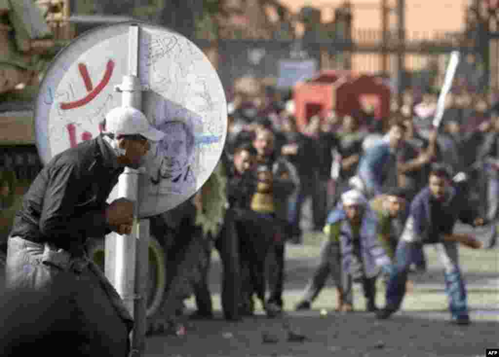 An anti-government protestor shelters behind a road sign pro-government demonstrators, background, throw rocks, in Cairo, Egypt, Wednesday, Feb.2, 2011. Several thousand supporters of President Hosni Mubarak, including some riding horses and camels and w