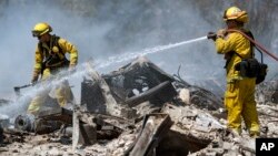 Carlos Orta, right, of Santa Cruz Calfire douses the smoldering remains of a home in Lower Lake, California, Aug. 15, 2016.