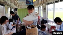 Seorang anggota staf organisasi menggendong seekor kucing di kafe kucing yang digelar di sebuah gerbong kereta di Jepang. Kampanye ini untuk meningkatkan kesadaran maraknya pemusnahan kucing di Jepang. 