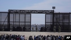 Des migrants qui ont traversé la frontière entre le Mexique et les États-Unis attendent à côté du mur frontalier américain où des agents de la patrouille frontalière américaine montent la garde, vus de Ciudad Juarez, Mexique, le 30 mars 2023.