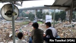 Rain, Satria, dan Cepi memandangi pemukimannya yang telah digusur, sesaat sebelum berangkat sekolah, Senin (16/12) siang. (VOA/Rio Tuasikal)