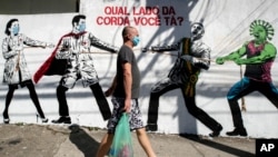 A man wearing a protective face mask walks past a mural depicting a tug-of-war between health workers and Brazil's President Jair Bolsonaro aided by a cartoon-styled coronavirus character, in Sao Paulo, Brazil, June 19, 2020.