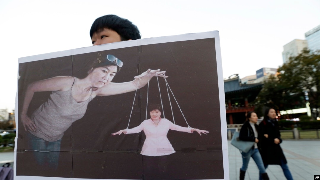 Seorang mahasiswa Korea Selatan membawa plakat bergambar Presiden Park Geun-hye (kanan bawah) sebagai boneka 'marionette' dan Choi Soon-sil (tengah) sebagai dalang dalam sebuah aksi demo di Seoul, Korea Selatan, 3 November 2016 (Foto: dok). Choi Soon-sil, menolak untuk hadir di hadapan komisi Majelis Nasional, Rabu (7/12).