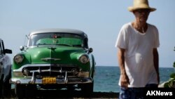 FILE - A man walks beside a U.S.-made car parked near the seaside on the outskirts of Havana.