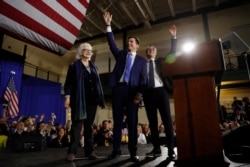 Democratic presidential candidate Pete Buttigieg, center, his husband, Chasten Buttigieg, and his mother, Anne Montgomery, stand on stage as supporters cheer at a primary night rally at Nashua Community College in Nashua, N.H., Feb. 11, 2020.