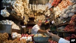 A vendor exchanges money with a customer at a shop selling garlic, onions and potatoes at a wholesale market in Mumbai (file photo)