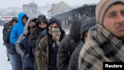 Migrants wait in line to receive plates of free food during a snowfall outside a derelict customs warehouse in Belgrade, Serbia, Jan. 18, 2017. 