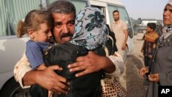 Abdul Rahman Ismail, an Iraqi soldier who has been targeted by Islamic State extremists who destroyed his house two years ago, is reunited with his family after they were able to flee their Islamic State held town, as displaced Iraqi families gather outside. (AP)