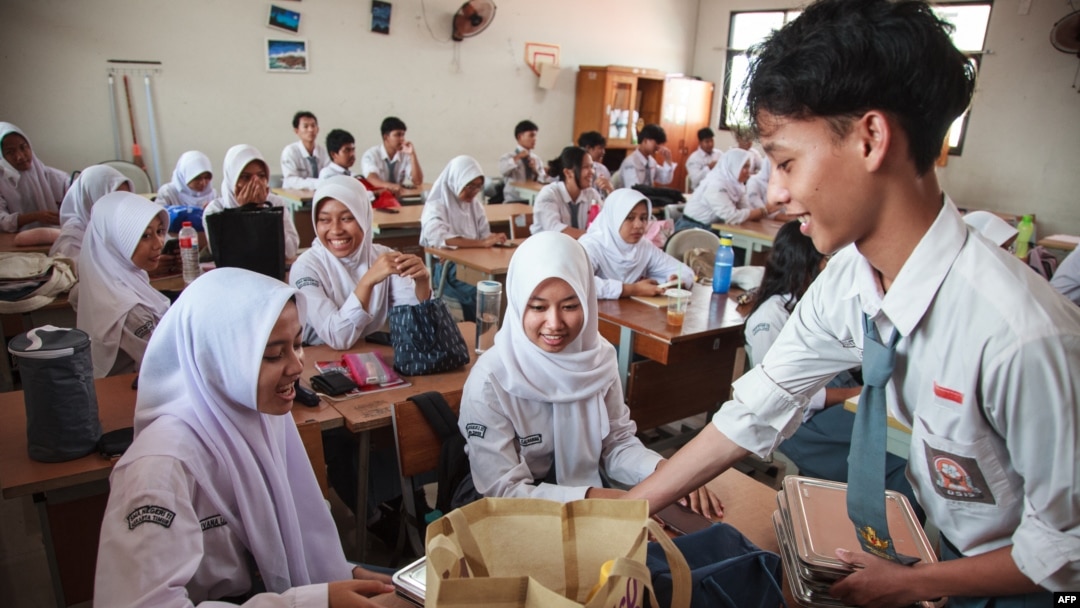 Para siswa menerima kotak makan siang pada hari pertama program makan gratis di SMA Negeri 11, Jakarta Timur, 6 Januari 2025. (Foto: AFP)