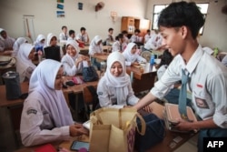 Siswa menerima kotak makan siang pada hari pertama program makan gratis di SMA Negeri 11, Jakarta Timur, 6 Januari 2025. (Foto: AFP)