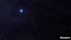 FILE - A meteor of the Orionid meteor shower, created by remnants of Halley's Comet, streak through the night sky past Halley's Comet, above the San Rafael Swell outside Green River, Utah, Oct. 23, 2019. 