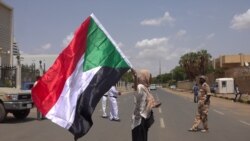 Hiba Salah waves Sudan’s flag outside Friendship Hall as the agreement is being signed (E. Sarai/VOA)