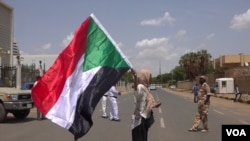 Hiba Salah waves Sudan’s flag outside Friendship Hall as the agreement is being signed (E. Sarai/VOA)