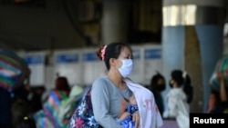 FILE PHOTO: A woman wearing a mask carries a baby at a bus station during the coronavirus disease (COVID-19) outbreak, in Bangkok