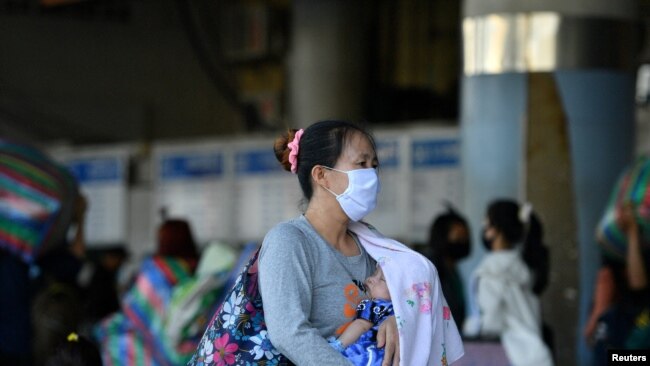 A woman wearing a face covering carries a baby at a bus station after many workers were around the station to return to their cities after many activities have been closed due to coronavirus disease (COVID-19) outbreak, in Bangkok, Thailand on March 22, 2020. (REUTERS/Challinee Thirasupa/File Photo)