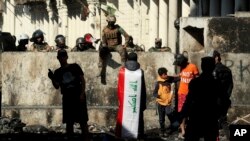 Iraqi security forces and anti-government protesters rest after both sides shake hands and converse in a rare moment of calm in hostilities, called to allow time for rest after clashes in Baghdad, Nov. 30, 2019.