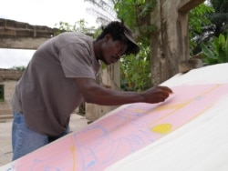 Sel Kofiga paints a piece of fabric he bought at Kantamanto market, in Accra, Ghana, Sept. 22, 2020. (Stacey Knott/VOA)