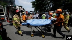 Firefighters and rescue team members carry a injured man who set himself on fire during an anti-Japan rally demanding full compensation and an apology for wartime sex slaves from the Japanese government in front of the Japanese Embassy in Seoul, South Korea, Aug. 12, 2015.