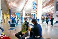FILE - Austin Kennedy, left, a Seattle Sounders season ticket holder, gets the Johnson &amp; Johnson COVID-19 vaccine at a clinic in a concourse at Lumen Field, May 2, 2021.