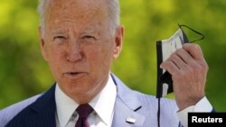 U.S. President Joe Biden pulls off his face mask as he arrives to speak about loosening coronavirus mask guidelines, outside the White House in Washington, April 27, 2021.