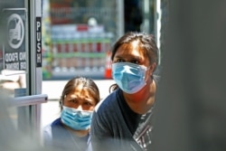 Two women peer into a clothing store to see if it is open, June 8, 2020, in the Sunset Park neighborhood of the Brooklyn borough of New York.