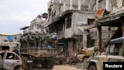 Truk militer yang penuh dengan tentara pemerintah melewati rumah-rumah dan gedung-gedung yang rusak seiring dengan berlanjutnya penyerangan terhadap militan pendukung ISIS. yang merebut distrik Mapandi di Kota Marawi, Filipina, 13 September 2017. 