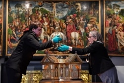 Director Birgitta Falk, right, and conservator Luke Jonathan Koeppe remove the top of the Saint Corona shrine at the Cathedral Treasury in Aachen, Germany, April 9, 2020. There is no relationship between St. Corona and coronavirus.
