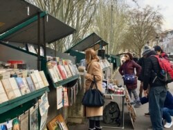 People look at goods being sold at the iconic kiosks by the Seine River in Paris. (Lisa Bryant/VOA)