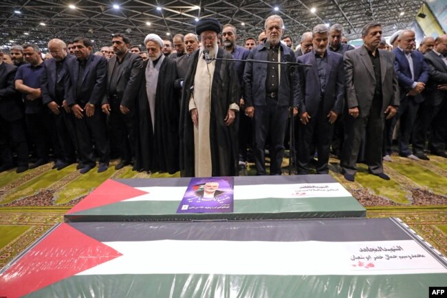 Pemimpin tertinggi Iran Ayatollah Ali Khamenei memimpin salat jenazah bersama Presiden Iran Masoud Pezeshkian (tengah-kanan) di atas peti jenazah mendiang pemimpin Hamas Ismail Haniyeh dan pengawalnya. (Foto: AFP)
