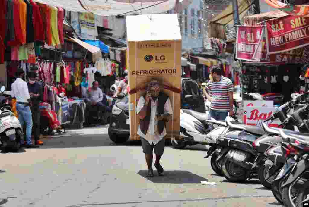 An Indian laborer talks on his mobile phone as he transports a refrigerator on his back at a market in Jammu.