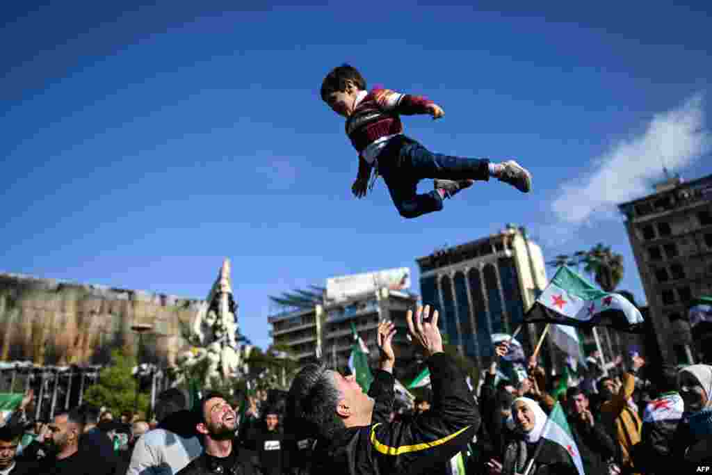 A man joyfully tosses a boy into the air as people gather at Saadallah al-Jabiri Square after the Friday noon prayers in Aleppo to celebrate the ousting of president Bashar al-Assad.