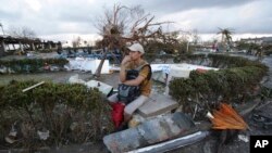 A man sits in the debris with an uprooted tree seen in background, after powerful typhoon Haiyan slammed into Tacloban, central Philippines on Saturday, Nov. 9, 2013.