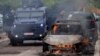Agentes de las fuerzas policiales de Kosovo actúan en medio de enfrentamientos con manifestantes de la población serbia en esa nación, mientras un automóvil se incinera, en el pueblo de Zvecan, el viernes 26 de mayo de 2023.