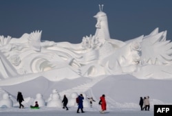 Visitors walk in front of an ice sculpture ahead of the opening of the Harbin International Snow and Sculpture Festival in Harbin, in China's northeast Heilongjiang province, Jan. 4, 2020.