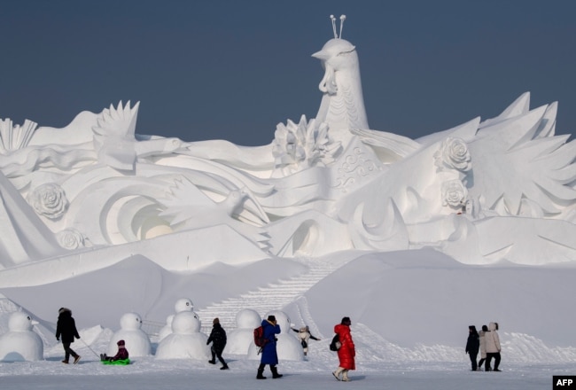 Visitors walk in front of an ice sculpture ahead of the opening of the Harbin International Snow and Sculpture Festival in Harbin, in China's northeast Heilongjiang province, Jan. 4, 2020.