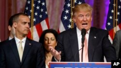 FILE - -In this March 15, 2016 file photo, Donald Trump's campaign manager Corey Lewandowski listens at left as Trump speaks in Palm Beach, Fla. 