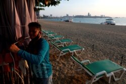 FILE - A man collects his umbrellas on an almost empty beach that's usually crowed with tourists, amid the global coronavirus disease outbreak, in Pattaya, Thailand, March 27, 2020.