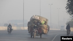 FILE PHOTO: Man rides a motor tricycle, loaded with sacks of recyclables, amid dense smog in Lahore