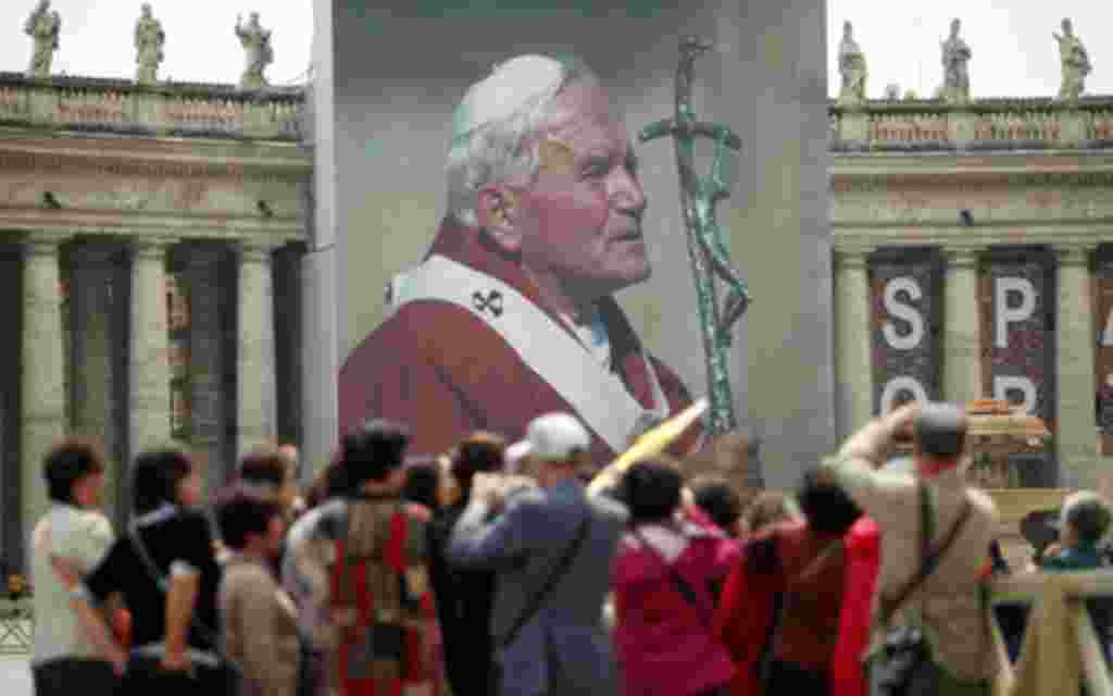 Los peregrinos esperan de pie delante de una imagen gigante del Papa Juan Pablo II en la Plaza de San Pedro en el Vaticano.
