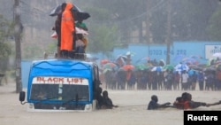 FILE— Passengers use a rope to wade through flood waters along a street, as they get evacuated from a public transport bus, following heavy rains in Kisauni district of Mombasa, Kenya November 17, 2023. 