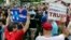 A supporter of Democratic presidential candidate Hillary Clinton and a Republican presidential candidate Donald Trump supporter hold signs as they attend a Memorial Day parade, May 30, 2016, in Chappaqua, N.Y.