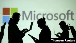 Las siluetas de usuarios de computadoras portátiles y dispositivos móviles se ven junto a una proyección de pantalla del logotipo de Microsoft en esta ilustración.