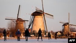 Skaters glide on the ice near windmills in the village of Kinderdijk, Netherlands.