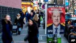 Ljudi prolaze pored izbornog plakata koji prikazuje njemačkog kancelara Olafa Scholza u Frankfurtu, Njemačka, 19. februar 2025. (Foto: AP/Michael Probst)