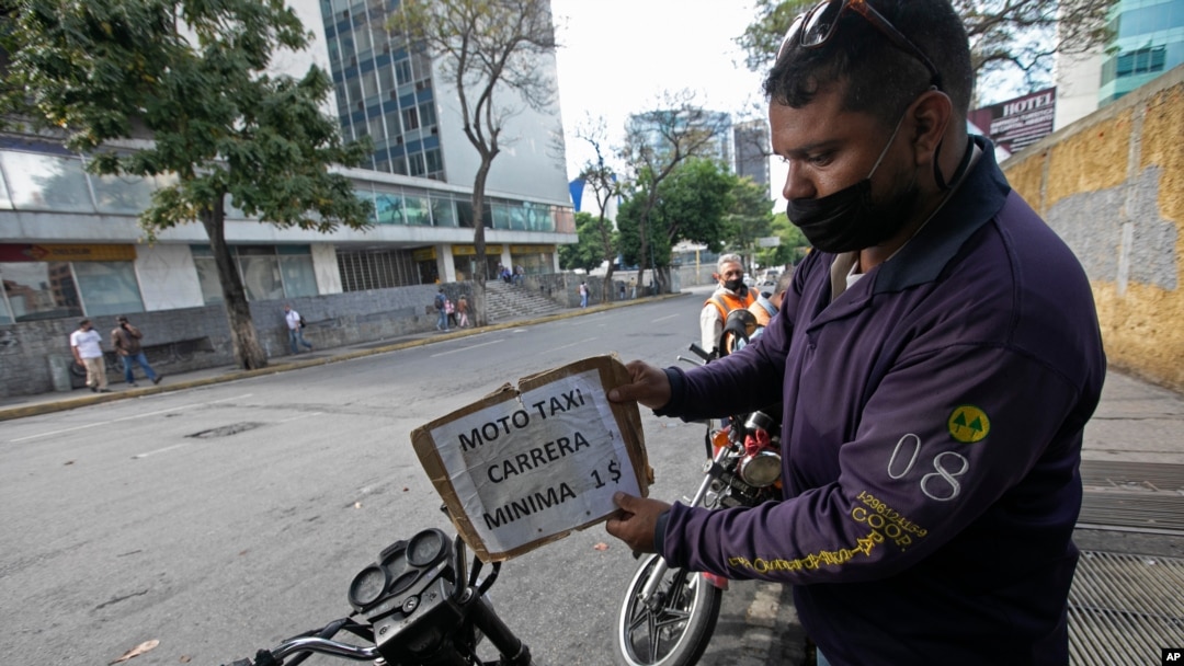 Un conductor de mototaxi coloca un cartel de precio que dice "mínimo un dólar" en Caracas, Venezuela. Junio 1, 2020.